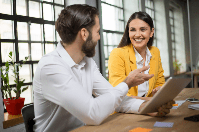 a man and woman sit in front of a laptop smiling at each other