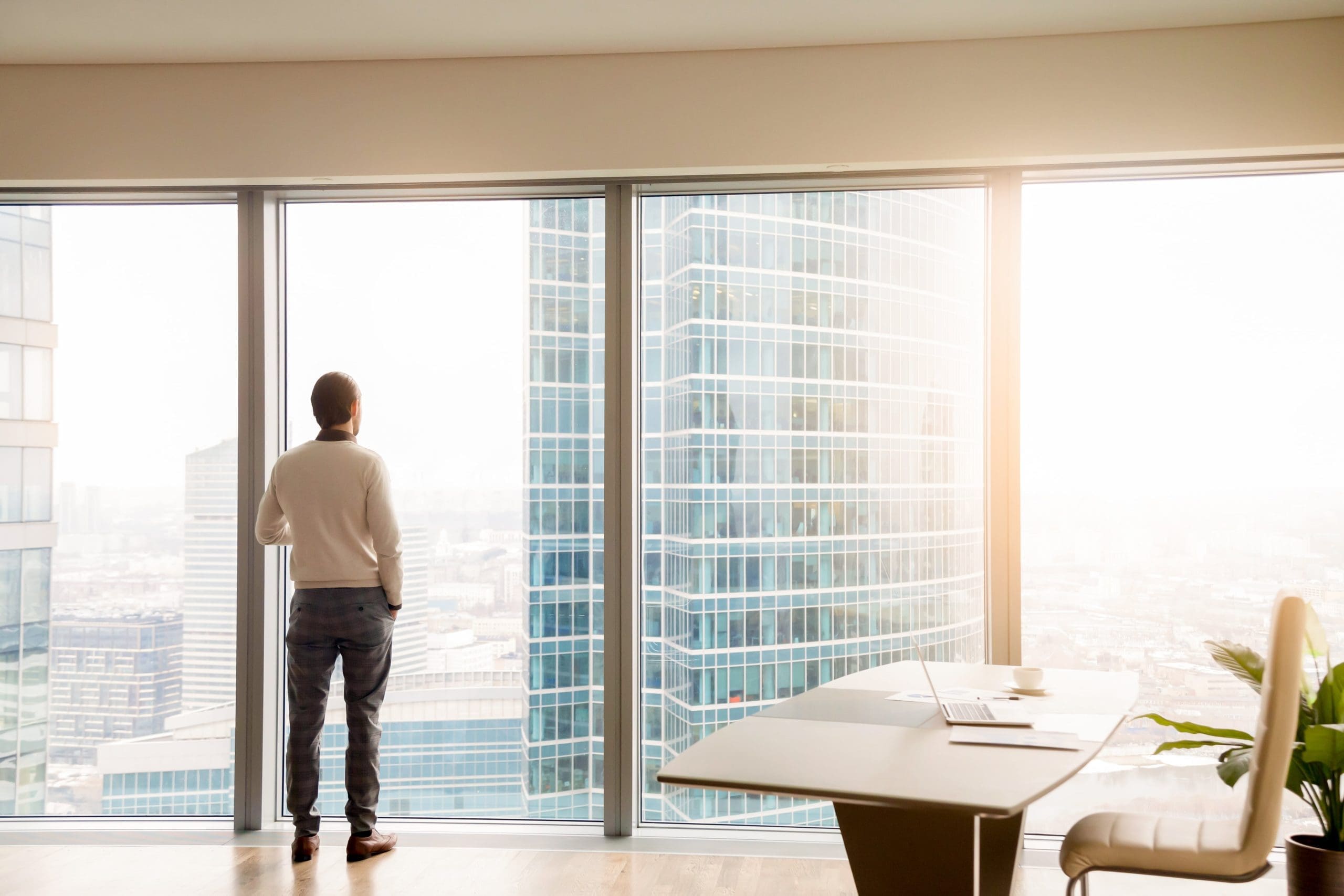 Business owner looking out window in high-rise office, reflecting on future exit strategy