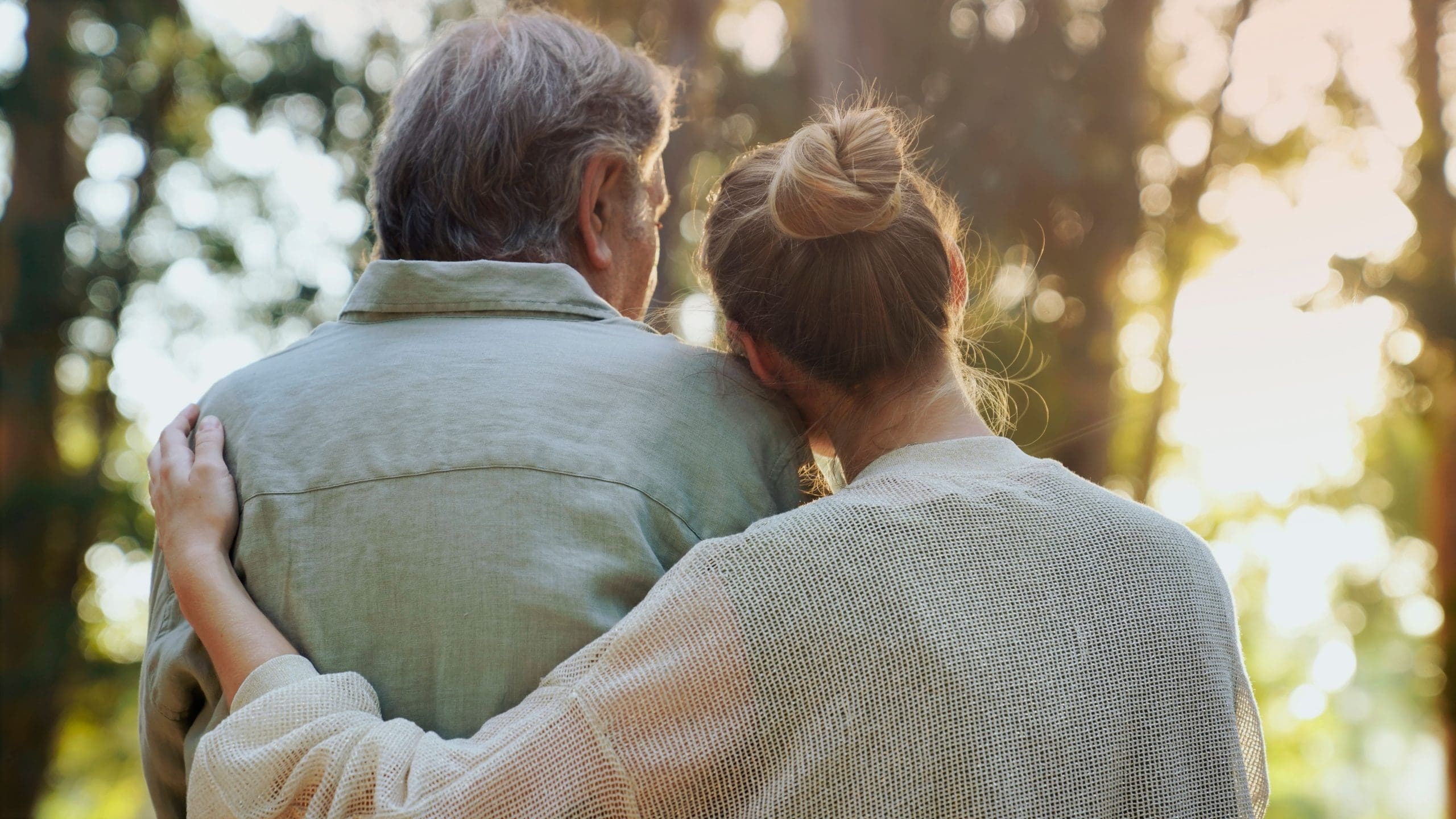 Daughter with her arm around her elderly father, sitting close together outdoors and sharing a quiet moment.