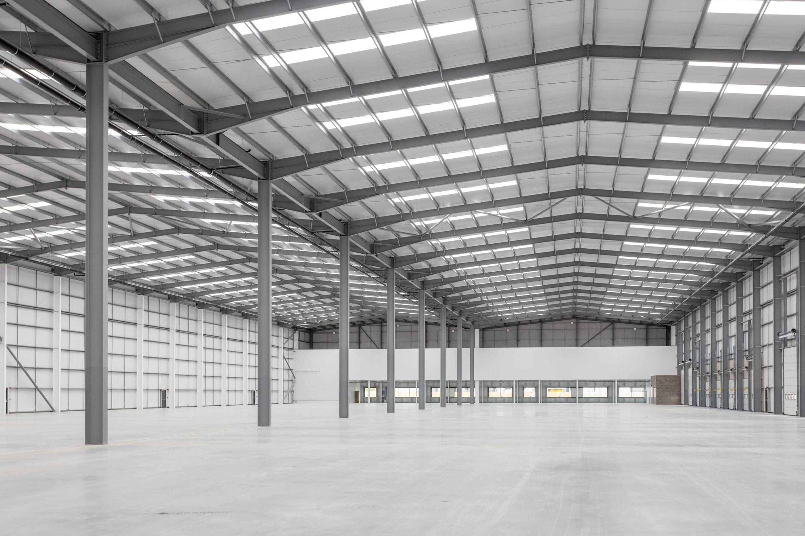 Interior view of a large commercial property warehouse with steel framework and ample natural light from the skylights.
