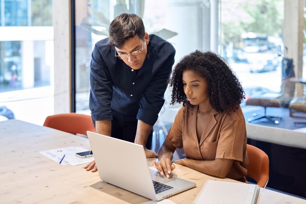 Two colleagues reviewing employment law guidance on a laptop, discussing pay, probation, and fixed-term contract reforms.