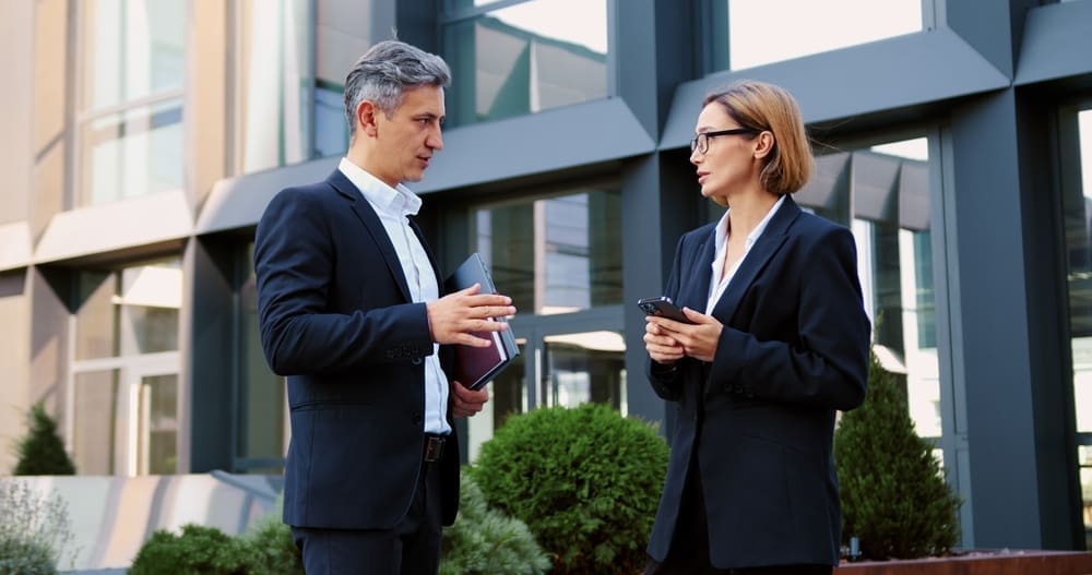 Two business professionals discussing financial matters outside a commercial office building, possibly related to receivership or property-backed lending, emphasizing the importance of strategic asset management in challenging economic conditions.
