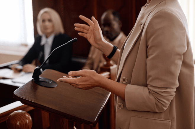 an image of a womans hands at a tribunal appeal, she is wearing a beige jacket and behind her are two people blurred in the background