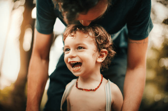 a smiling child with their father standing behind them blurred out